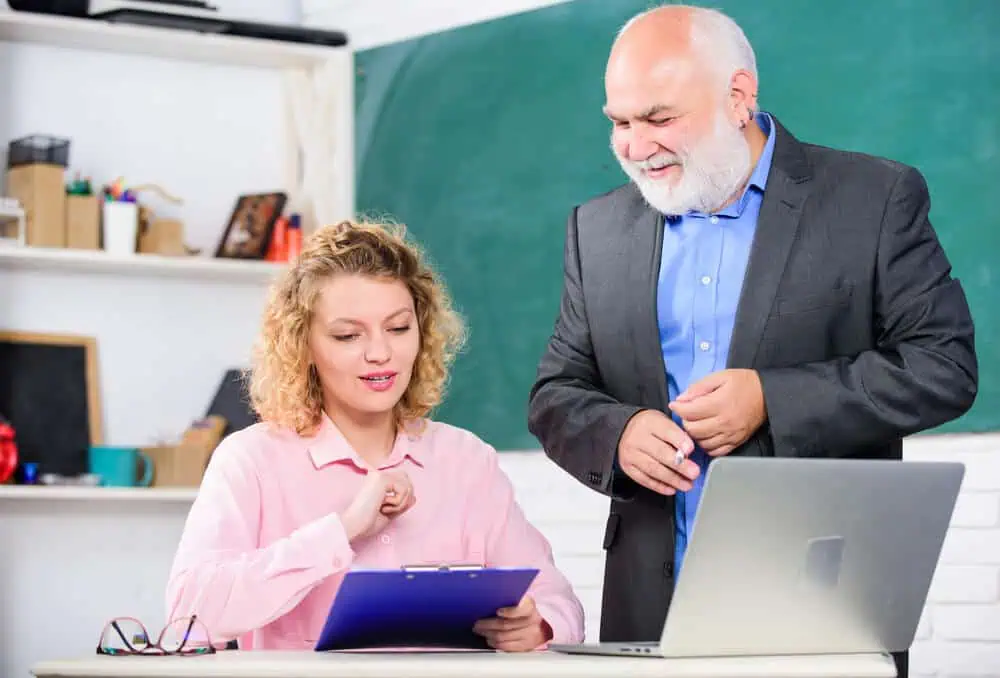 Teacher and student collaborating in a classroom with a laptop and tablet.