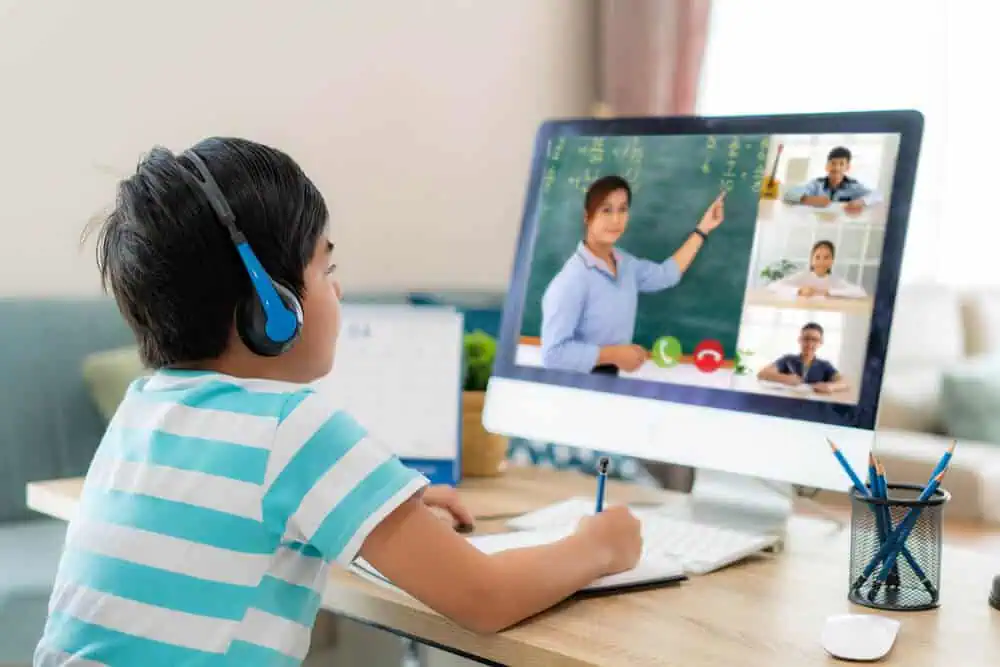 Student engaging in online learning via video call with a teacher on a computer screen.