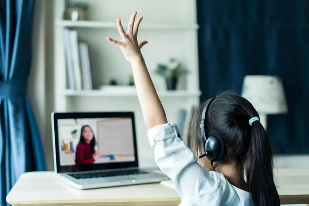 Young student engaging in online learning with headset and raised hand during virtual class.