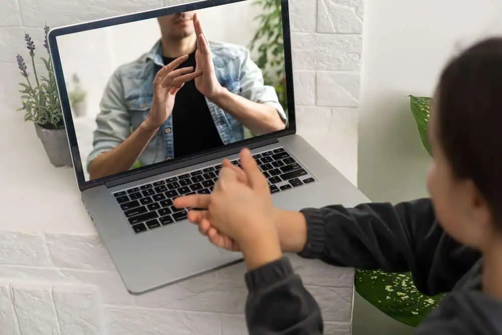 Child engaging in online learning via video call with a teacher on a laptop.