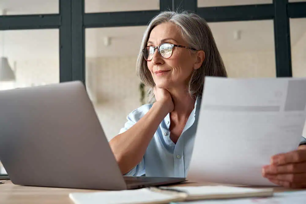 Woman studying online with laptop and papers, engaging in remote learning.