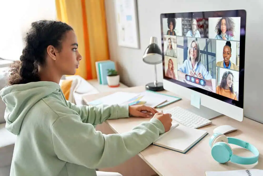 Student participating in a virtual classroom with multiple teachers via computer screen.