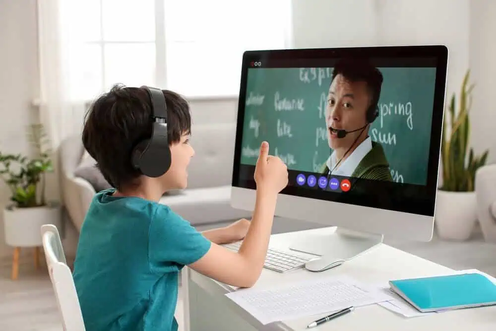Child engaging in virtual learning with a teacher via computer headset.