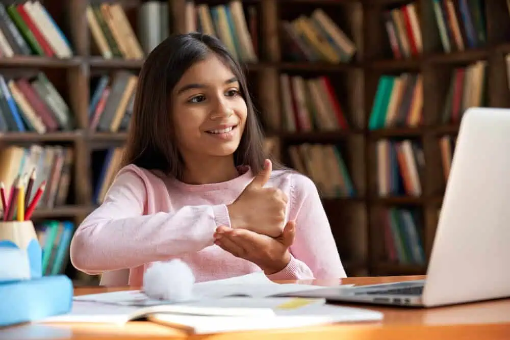 Young girl engaging in online learning with a laptop in a library setting.