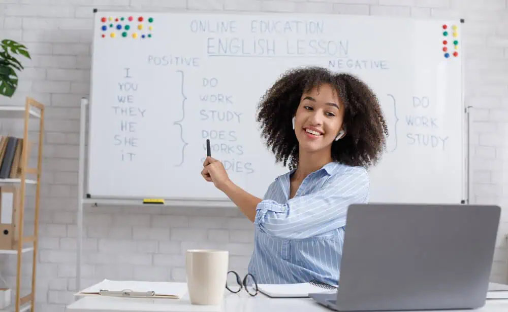 Young woman teaching online English class with whiteboard and laptop.