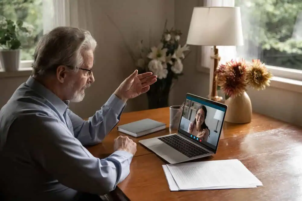 Senior man engaging in a virtual learning session with a teacher on a laptop.