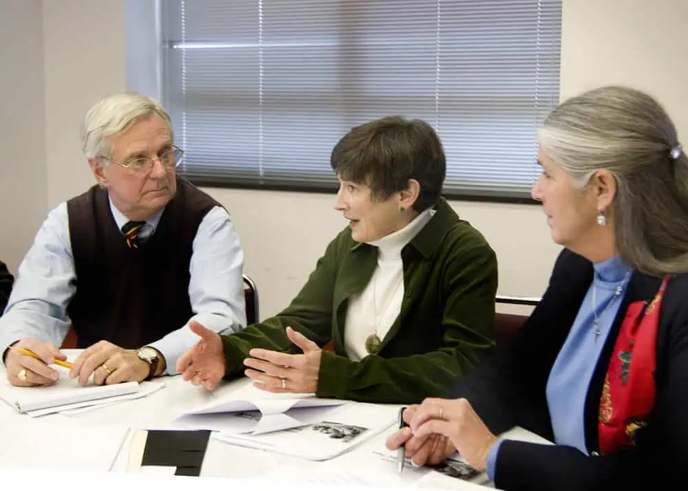 Three adults engaged in a professional discussion at a meeting table.