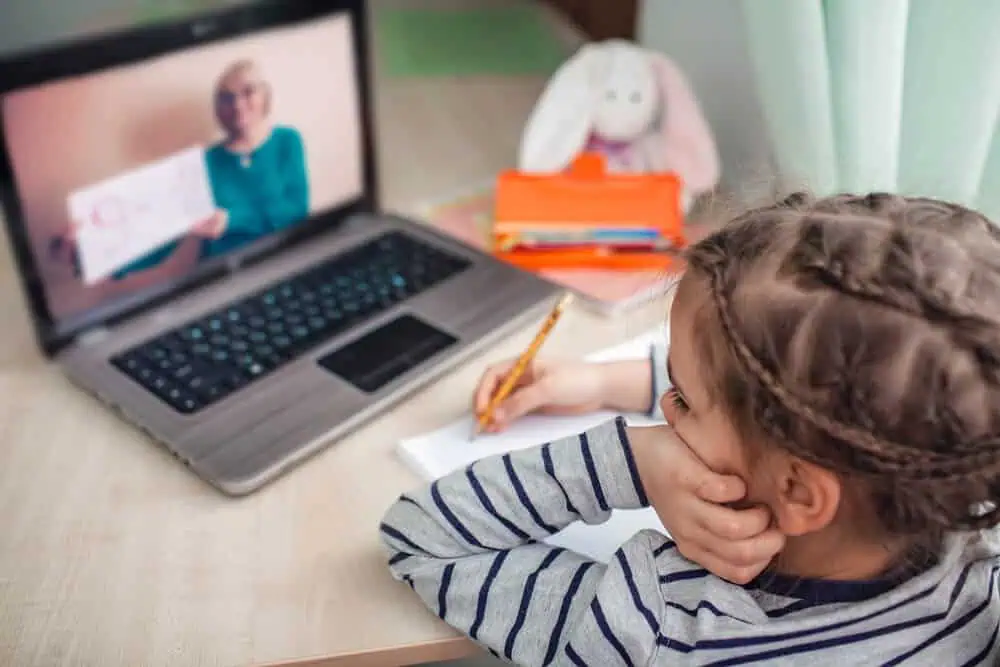 Child attending virtual class with a teacher on a laptop for remote learning.