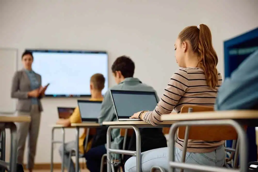Students attending an online class with a teacher via digital platform in a classroom setting.