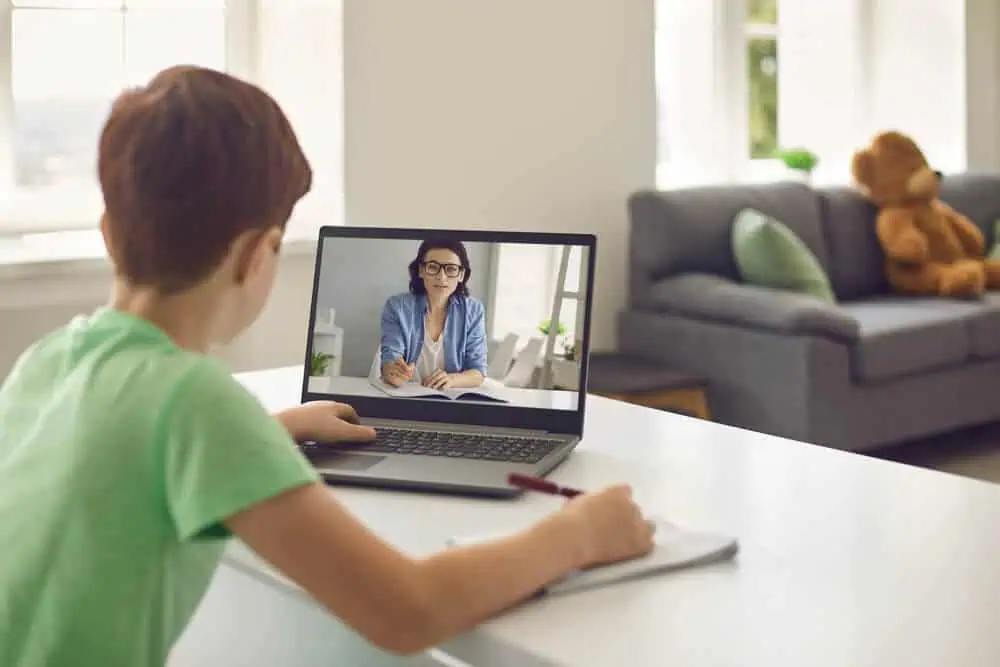 Student participating in a virtual classroom with a teacher via laptop at home.
