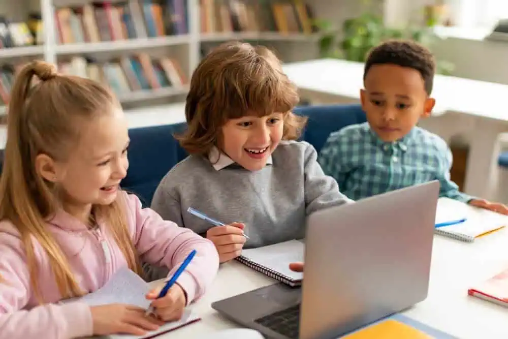 Children engaging in online learning with a laptop in a classroom setting.