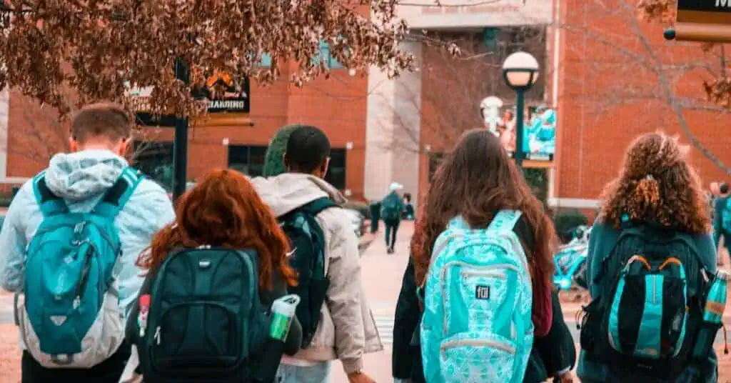 Group of students with backpacks walking outdoors in a school campus setting.