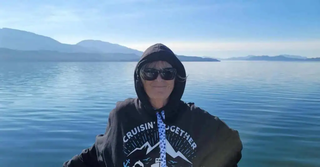 Woman in sunglasses on a boat with a lake and mountains in the background.