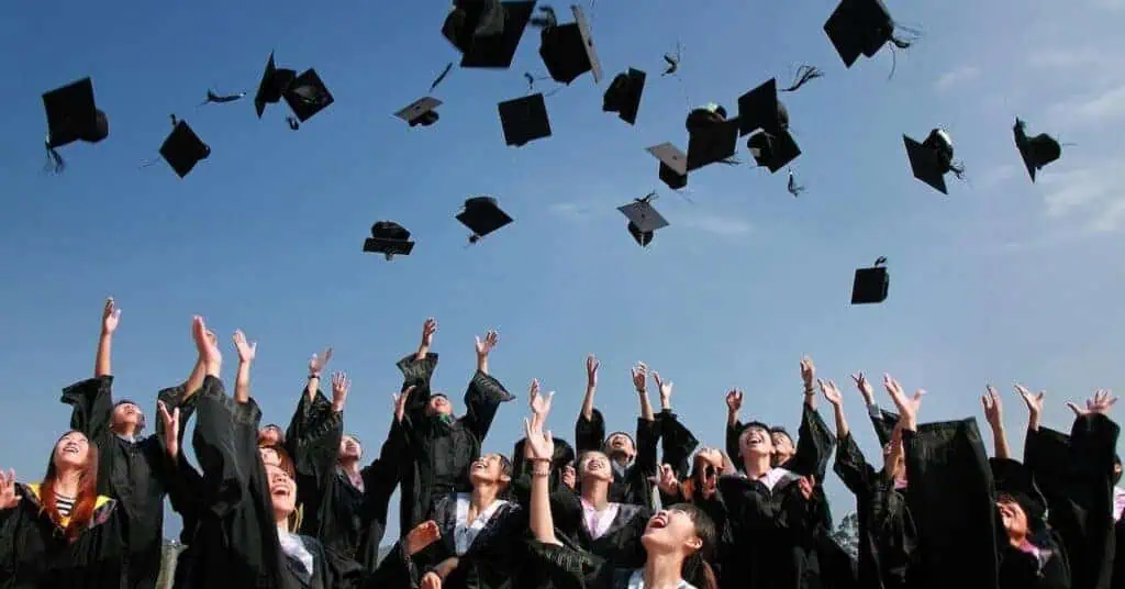 Graduates celebrating at a graduation ceremony, tossing caps in the air outdoors.