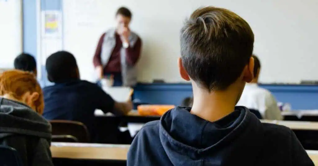 Student attentively listening in a classroom with a teacher at the whiteboard.
