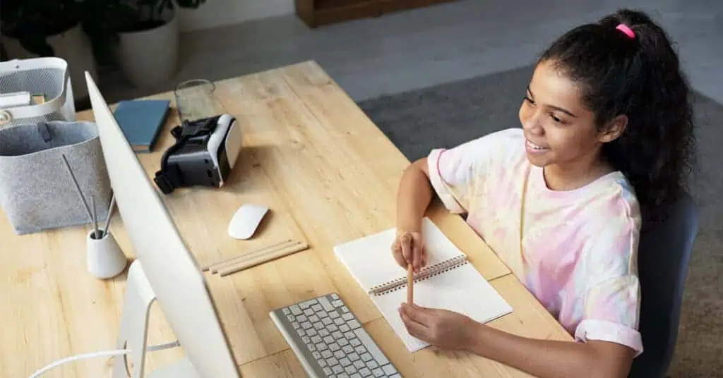 Young girl engaging in online learning with a computer and notebook.
