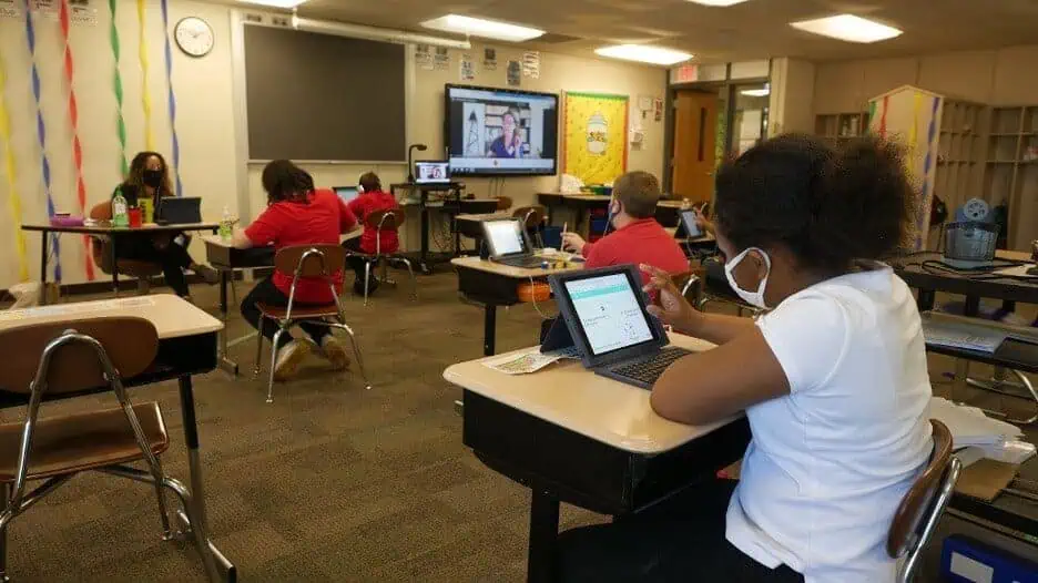 A certified virtual teacher leads a classroom lesson as students work on their laptops.