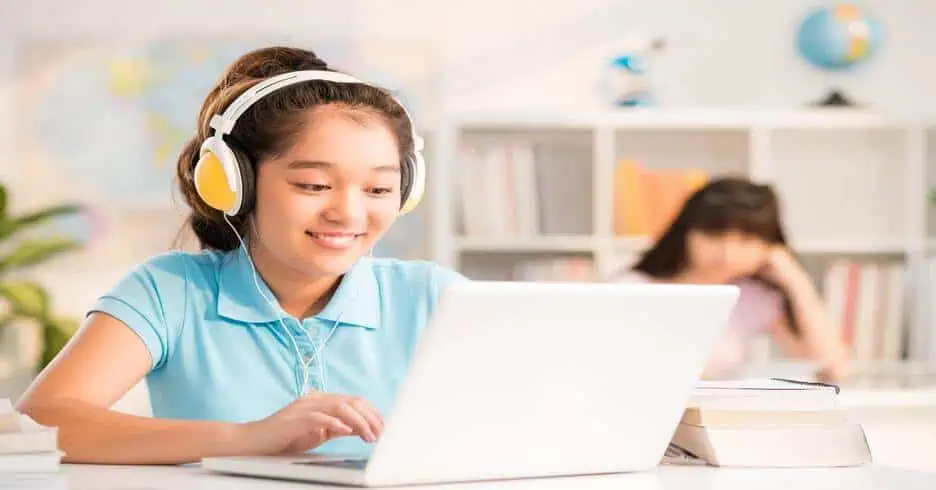 Young girl engaging in online learning with headphones and laptop in a classroom setting.