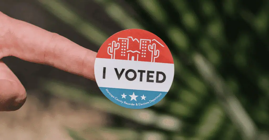Hand holding a "I VOTED" sticker with patriotic design, promoting civic engagement.