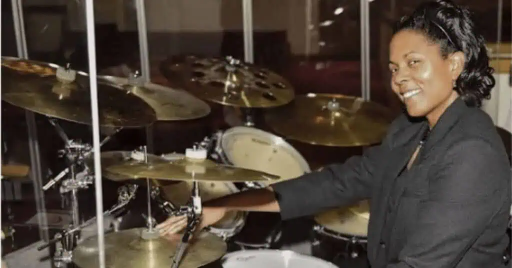 Female drum instructor playing drums in a music studio for remote learning.
