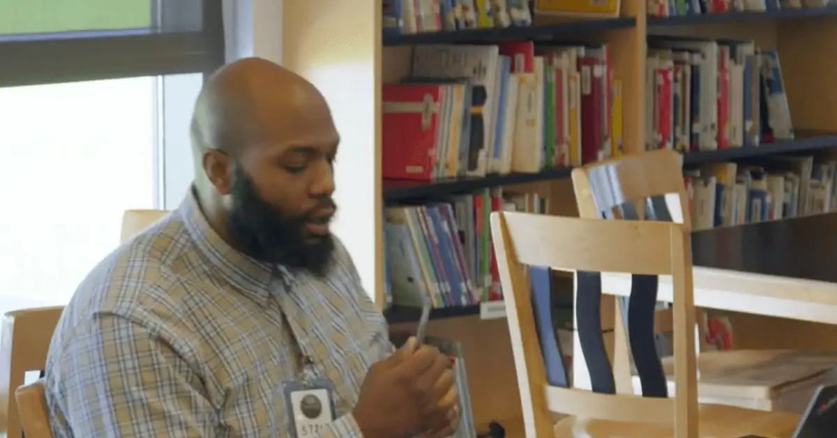 Adult male student using a tablet in a library setting for remote learning.