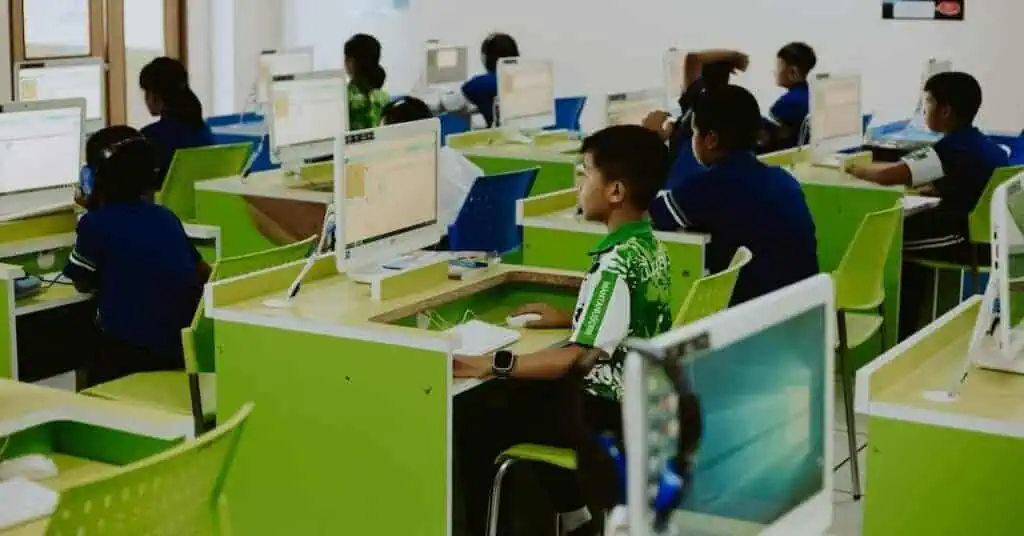 Students learning online in a modern classroom with computers and bright green desks.