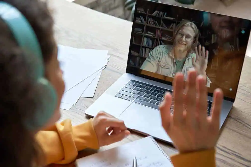 A student and an online synchronous teacher waving to each other virtually