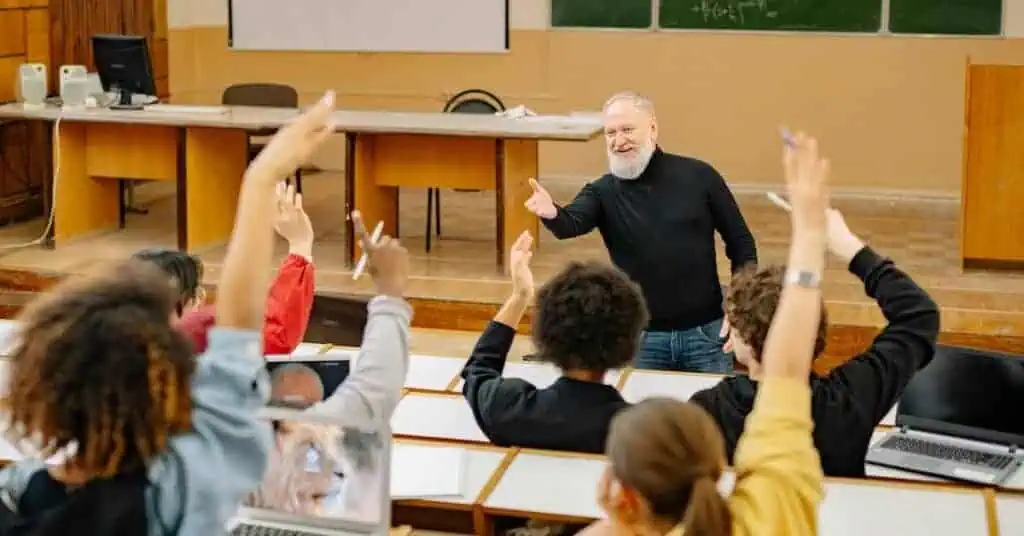 students raise hands in college classroom