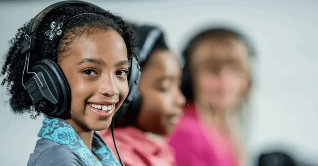 Student with headphones smiles while working alongside other students in computer lab