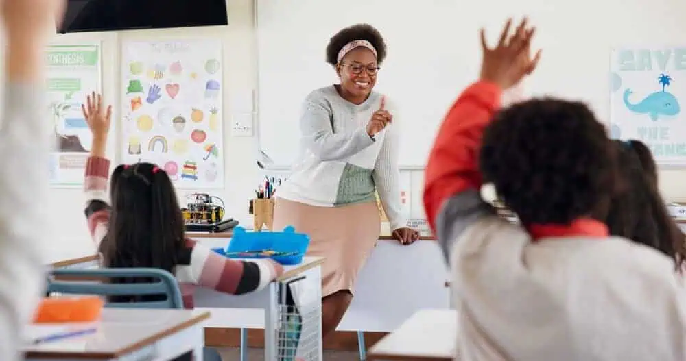 A female substitute teacher choosing students with hands raised for a question.