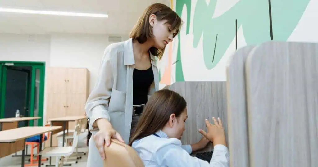 A teacher stands over her student’s shoulder
