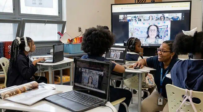 Students engaging in a virtual classroom with a teacher via video conference.