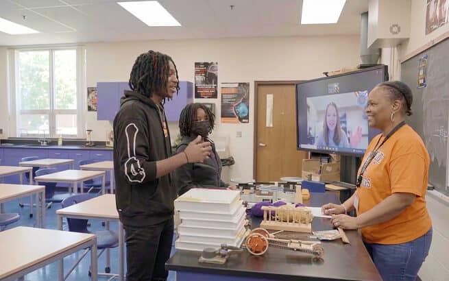Students engaging in a virtual classroom session with a teacher via video call.