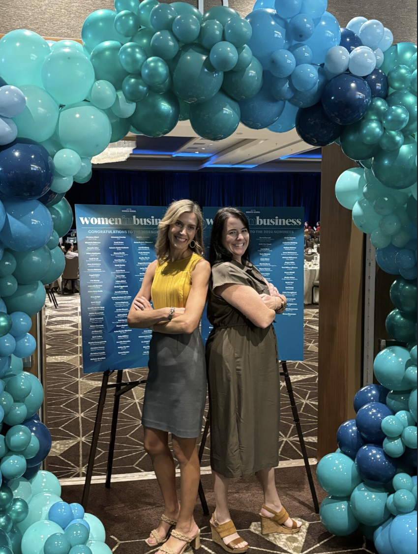 two women in business posing under an arch