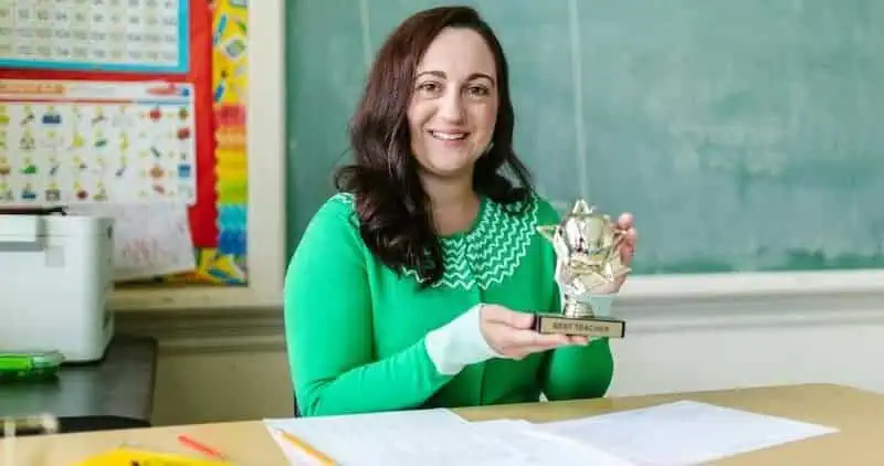 Female teacher holding an award trophy in a classroom setting.