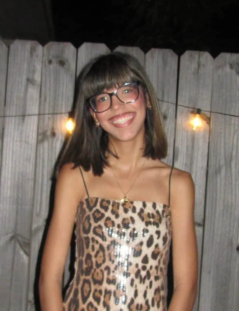 Young woman with glasses smiling, wearing leopard print dress at outdoor event.