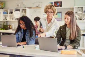 Teacher guiding students in a virtual classroom setting with laptops.