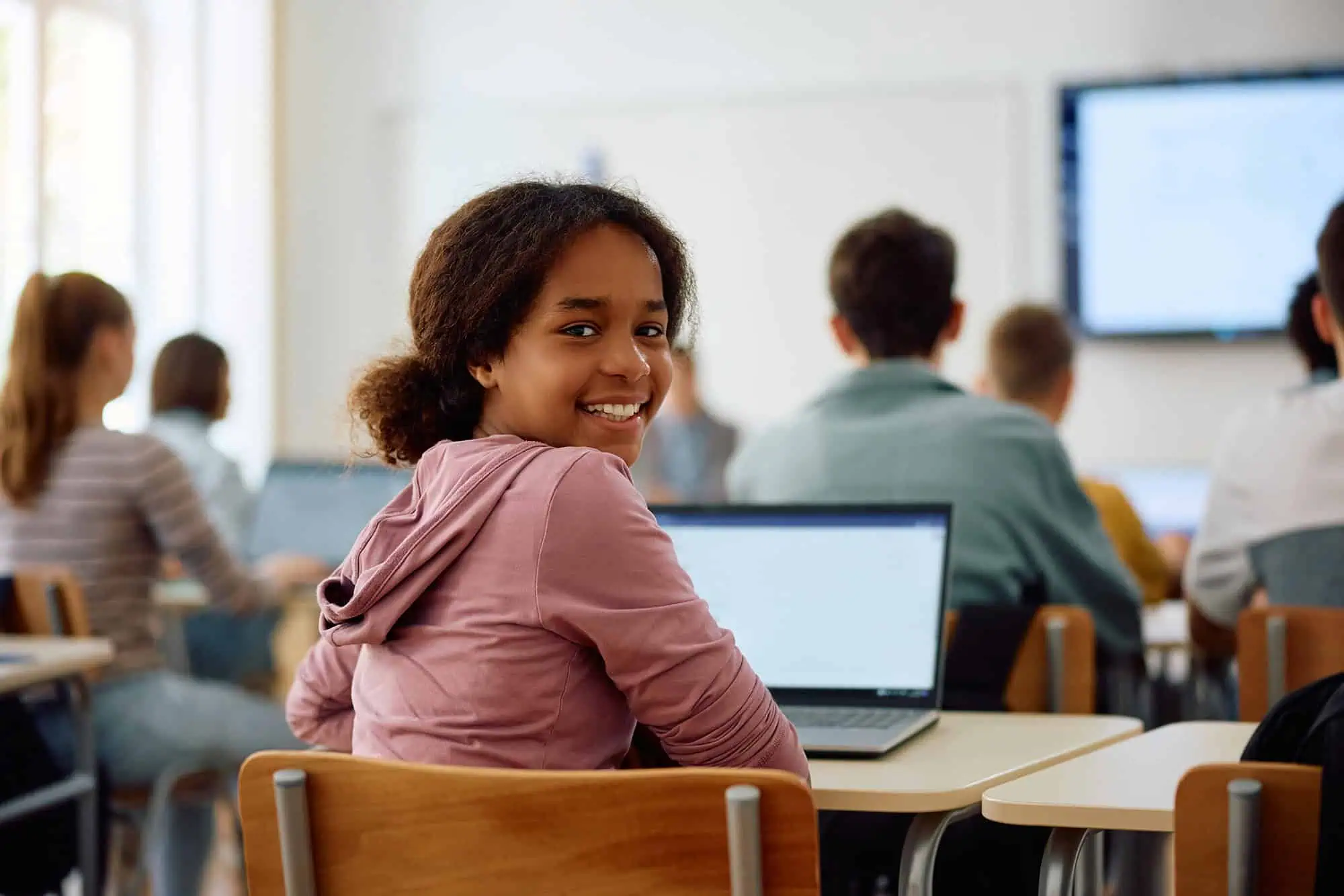 Smiling student in classroom with laptop during online learning.